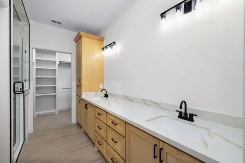 Double vanity with natural wood cabinets, black faucets and a walk-in closet
