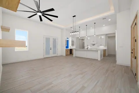 Open living room with a lit tray ceiling and wood-look tile, looking into the kitchen