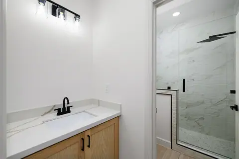 Wood vanity with a black faucet and a glass shower beyond