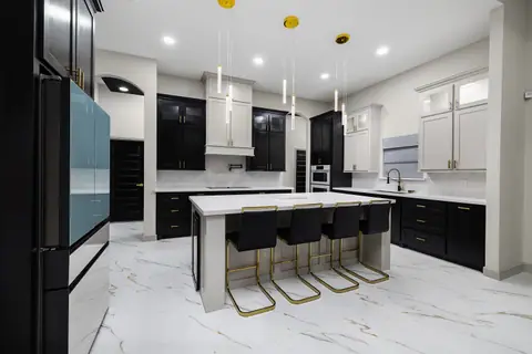 Cocina en dos tonos con gabinetes bajos negros, altos blancos e isla con bancos dorados