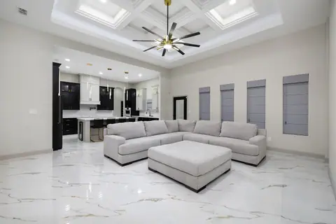Living room under a lit coffered ceiling, open to the kitchen