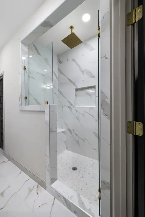 Glass walk-in shower with marble-look tile and a gold rain head
