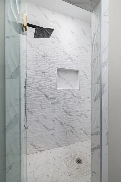 Shower with wave-textured wall tile and a black rain head