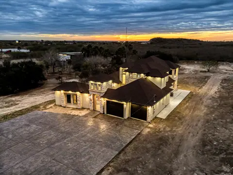 Aerial view at dusk of a two-story stone and stucco home with its lights on