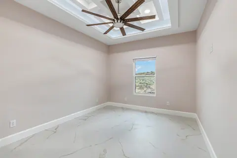 Bedroom with a lit tray ceiling, a ceiling fan and a marble-look tile floor
