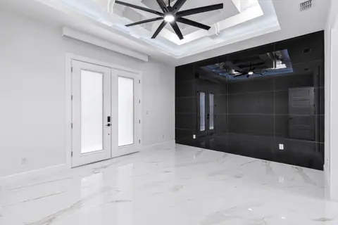 Room with a glossy black tile wall, French doors and a lit coffered ceiling