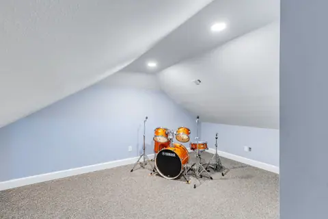 Carpeted bonus room under a sloped ceiling, set up as a music room