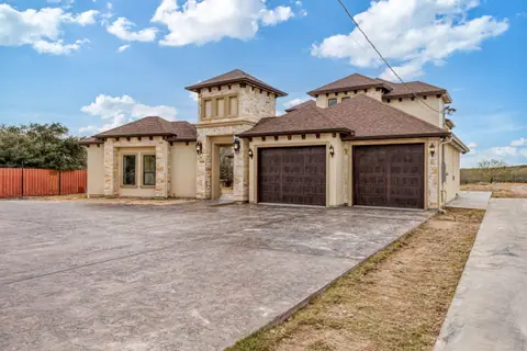 Stucco home with two wood-tone garage doors and a metal privacy fence behind it