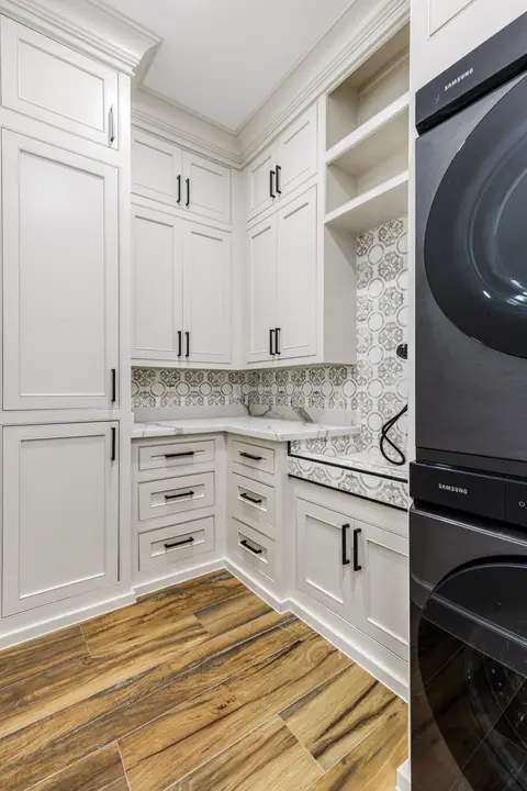 Cuarto de lavado con lavadora y secadora apiladas, gabinetes blancos y piso tipo madera