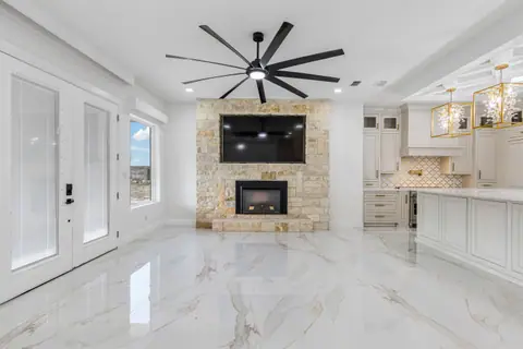 Stone fireplace with a mounted TV, a black ceiling fan and French doors to the patio