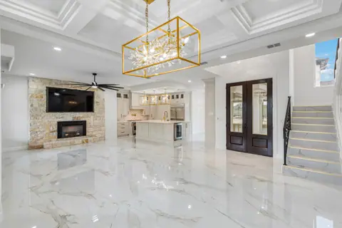 Open living room with a stone fireplace, coffered ceiling, marble-look tile and iron entry doors