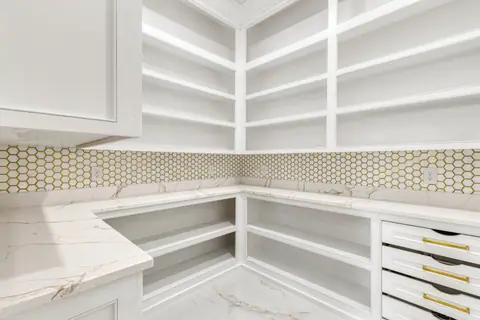 Walk-in pantry with open shelving, white counters and a hexagon mosaic backsplash