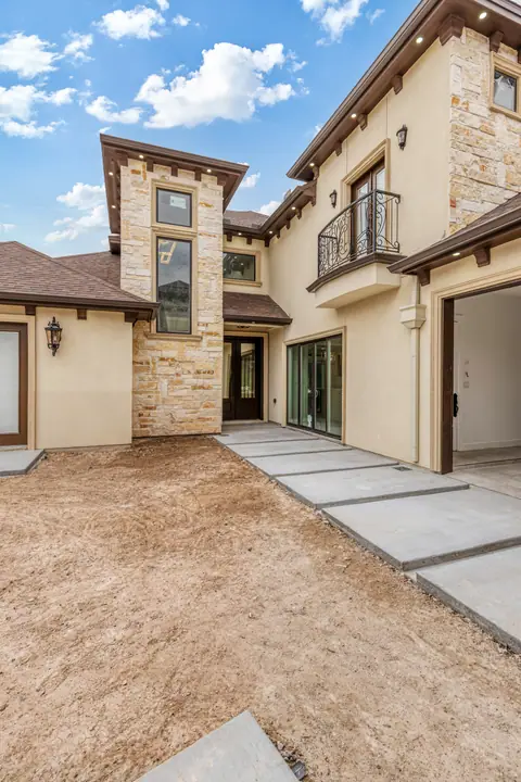 Side entry with concrete step pavers, stone accents and an iron balcony above