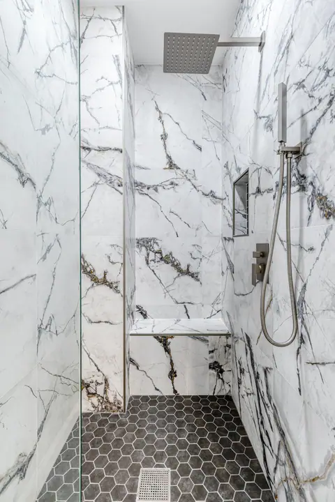 Walk-in shower with marble-look porcelain walls, a bench and a black hexagon floor