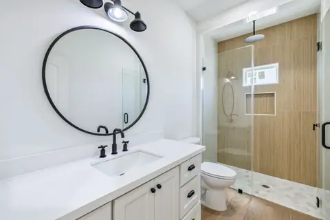 Bathroom with a round mirror vanity and a glass shower with wood-look tile