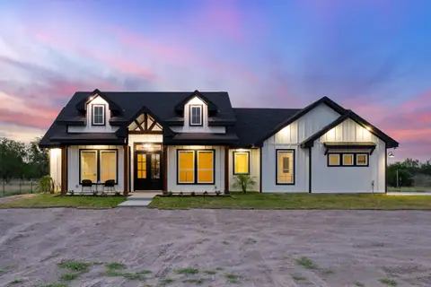 White farmhouse at dusk with lit windows, dormers and a covered front porch
