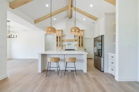 White kitchen island with woven pendant lights under vaulted wood beams