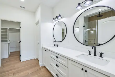 Double vanity with round black mirrors and a walk-in closet beyond