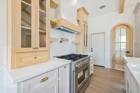 Gas range with a pot filler between natural wood glass-front cabinets